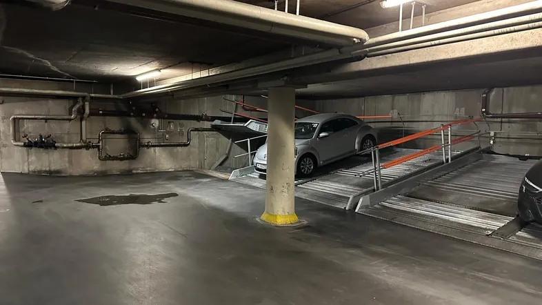 Tiefgarage mit Doppelparker-System und sichtbaren Versorgungsleitungen in einem Mehrfamilienhaus.