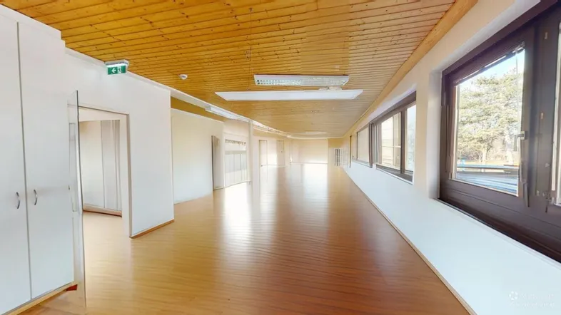 Geräumiger, leerer Büroraum mit Holzboden, Holzdecke und großen Fenstern für viel Tageslicht.