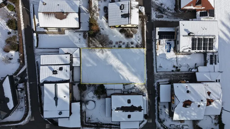 Luftaufnahme eines schneebedeckten Wohngebiets mit Häusern und einem markierten Grundstück.