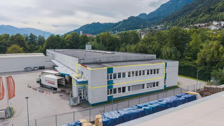 Luftaufnahme eines Gewerbegebäudes mit Laderampe und umliegender Berglandschaft unter bewölktem Himmel.