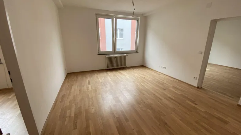 Helles, leeres Zimmer mit Parkettboden und weiß gestrichenen Wänden, bereit zur individuellen Gestaltung.