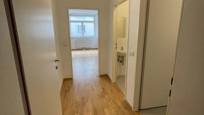 Heller Flur mit Holzparkettboden und Zugang zu verschiedenen Zimmern, inklusive Bad und Wohnbereich.