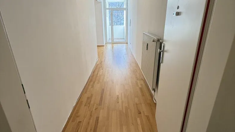 Heller Flur mit Holzparkettboden und Zugang zu einem Balkon, der viel Tageslicht hereinlässt.