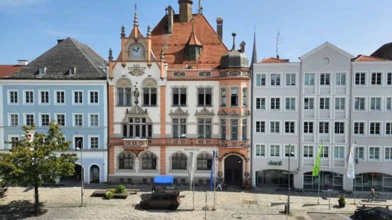 Historische Gebäudeansicht eines Marktplatzes mit Rathaus und umliegenden Häusern unter blauem Himmel.