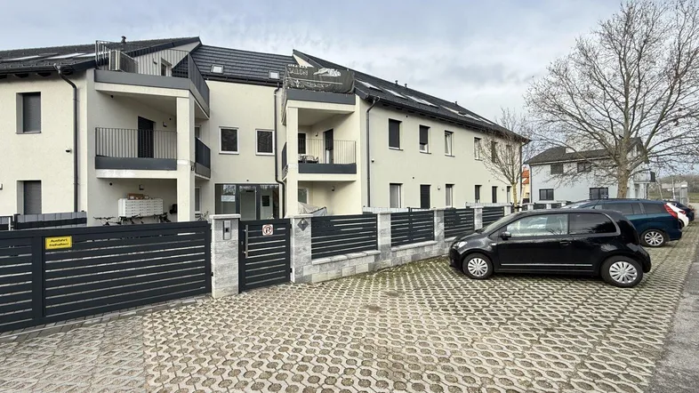 Moderne Wohnanlage mit Balkonen, Zaun und Parkplätzen unter bewölktem Himmel.