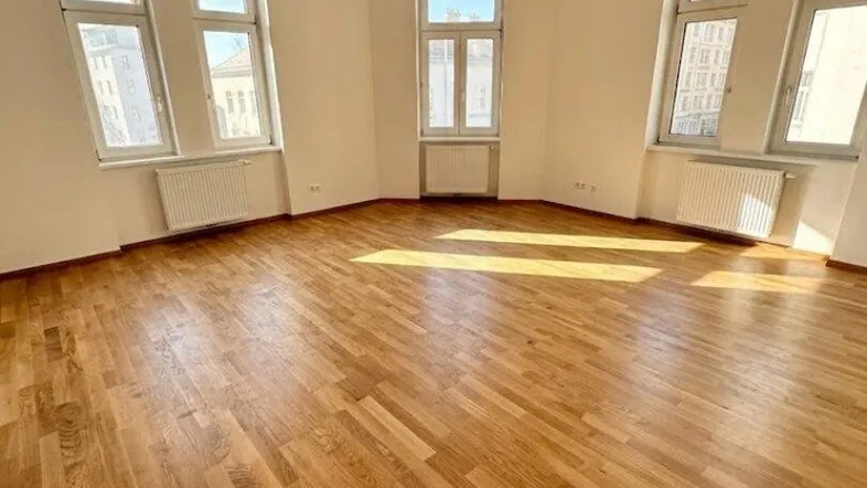 Helles Zimmer mit Fischgrätparkettboden und vielen Fenstern, ideal als Wohn- oder Schlafzimmer.