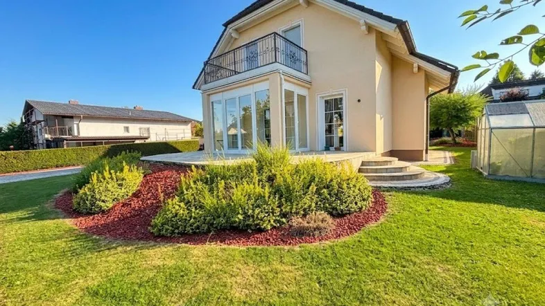 Haus mit Terrasse, Garten und Balkon unter blauem Himmel.