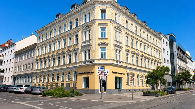 Historisches Eckgebäude mit gelber Fassade und vielen Fenstern in urbaner Umgebung.