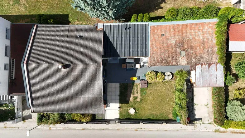 Luftaufnahme eines Hauses mit Garten, Terrasse und verschiedenen Dachformen in einer Wohngegend.
