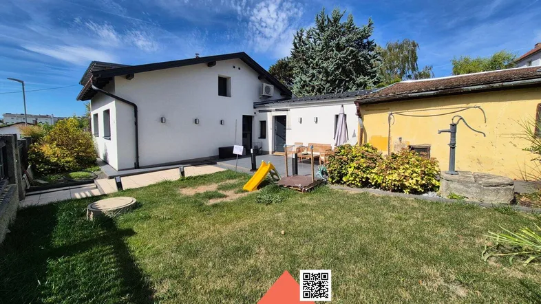 Hinterhof mit Rasenfläche, Kinderrutsche und einer kleinen Terrasse, umgeben von Sträuchern.