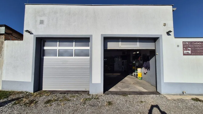 Fassade eines Gebäudes mit zwei Garagentoren, eines davon geöffnet, das den Innenbereich zeigt.