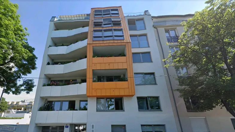 Modernes Mehrfamilienhaus mit weißer Fassade und markantem orangefarbenem Erker mit Balkonen.