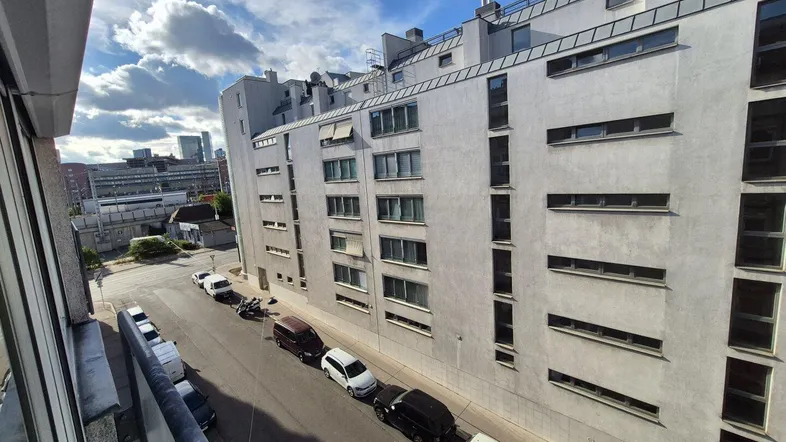 Blick von einem Balkon auf die moderne Fassade eines Wohngebäudes und die darunterliegende Straße.