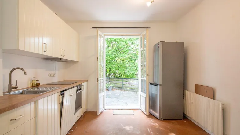 Küche mit cremefarbenen Einbauschränken, Holzarbeitsplatte und direktem Zugang zur Terrasse mit Grünblick.