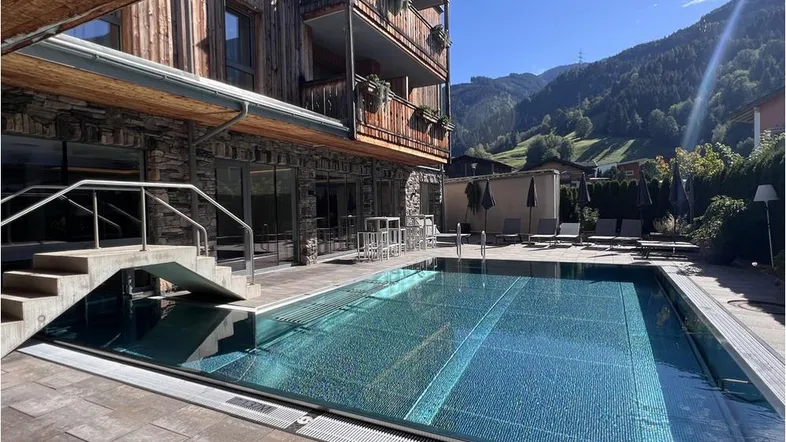 Außenbereich mit großem Pool, umgeben von einer Sonnenterrasse und alpiner Architektur.
