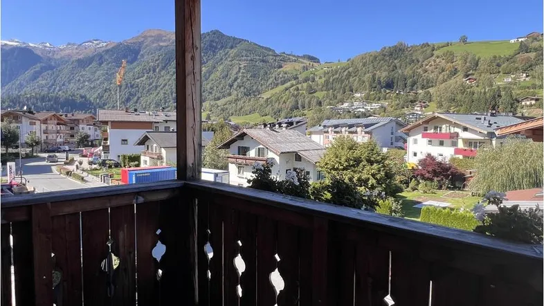 Panoramablick vom Holzbalkon auf das Dorf und die umliegenden Berge unter blauem Himmel.