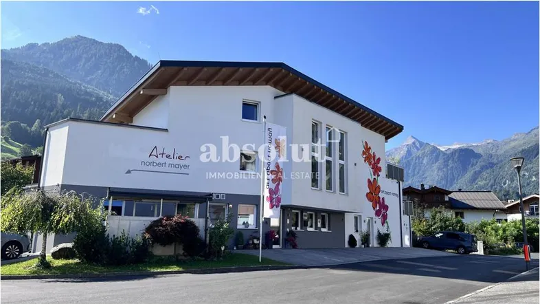 Modernes Gebäude mit weißer Fassade, bunten Blumenmotiven und Bergblick in sonniger Umgebung.