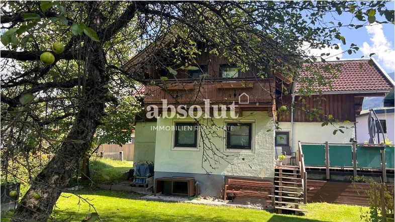 Charmantes Haus mit traditioneller Holzfassade und grünem Gartenbereich umgeben von Bäumen.
