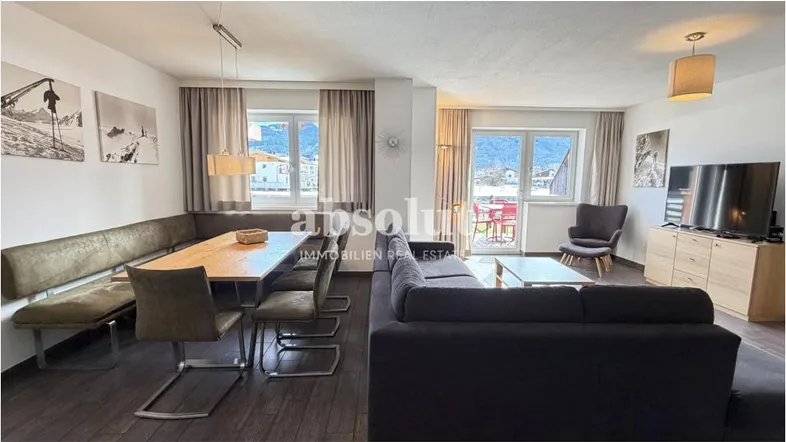 Gemütlicher Wohn-Essbereich mit dunklem Holzboden, bequemer Eckbank und Zugang zum Balkon.