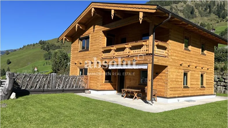 Traditionelles Holzhaus im Chalet-Stil mit gepflegtem Rasen und Bergblick unter blauem Himmel.