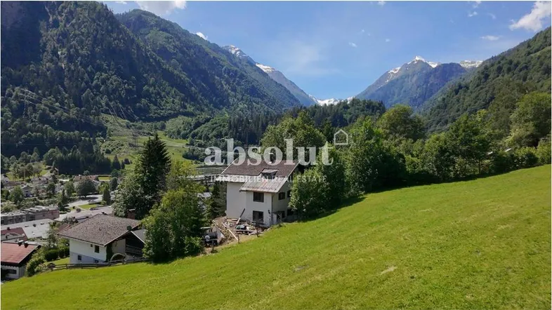 Haus in idyllischer Berglandschaft mit grünen Wiesen und schneebedeckten Gipfeln im Hintergrund