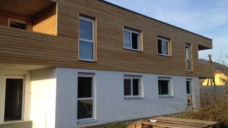 Modernes Mehrfamilienhaus mit Holzfassade und weiß verputztem Sockelbereich im Bau.