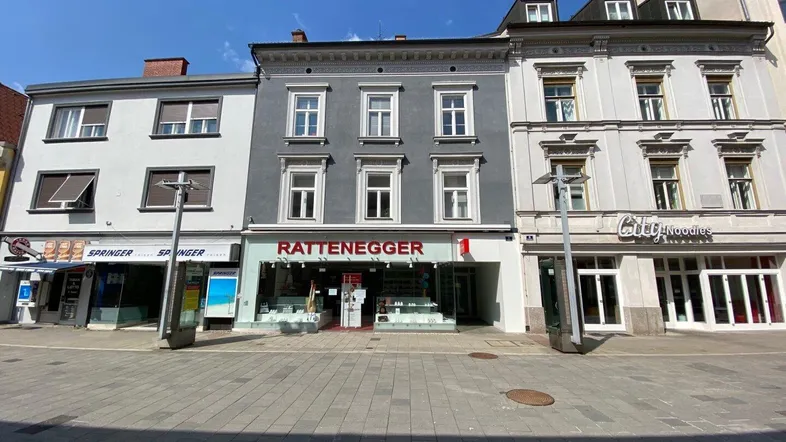 Fassade eines Mehrfamilienhauses mit Geschäften im Erdgeschoss in einer städtischen Umgebung.