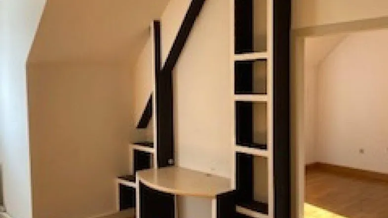 Helles Zimmer mit Holzboden und integriertem Regal-Schreibtisch-System unter der Dachschräge.