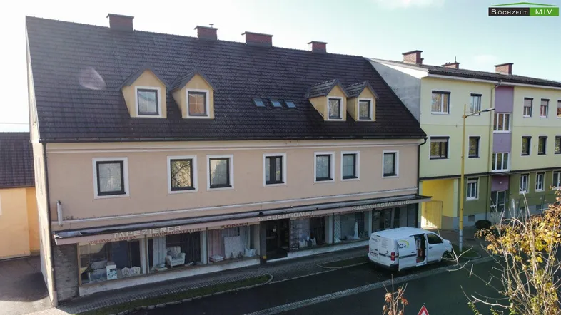 Mehrstöckiges Gebäude mit Geschäftsräumen im Erdgeschoss und Wohnungen darüber, an einer Straße gelegen.