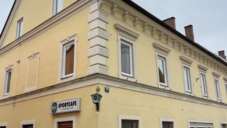 Gelbes Eckgebäude mit traditioneller Architektur und einem Sportcafé im Erdgeschoss an einer Straße.