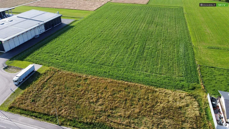 Luftaufnahme von landwirtschaftlichen Feldern, einem Gewerbegebäude und einer Straße mit LKW.