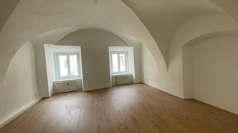 Geräumiger Raum mit einzigartiger Gewölbedecke, Holzboden und zwei Fenstern, die viel Licht hereinlassen.