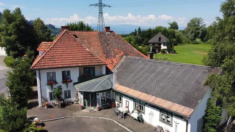 Luftaufnahme eines traditionellen Gebäudekomplexes mit rotem Ziegeldach, umgeben von grüner Landschaft und Bergen.
