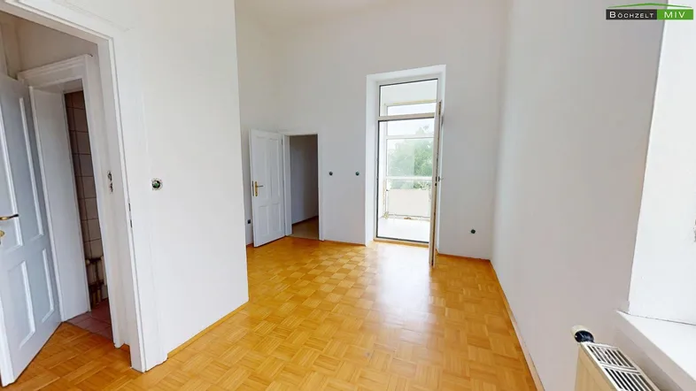 Helles Zimmer mit Parkettboden und Zugang zu einem Balkon, ideal als Wohn- oder Schlafbereich.