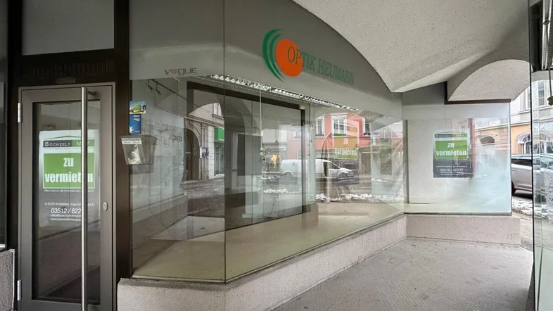 Blick auf die Ladenfront eines Optikergeschäfts mit großen Schaufenstern und einem "Zu vermieten"-Schild.