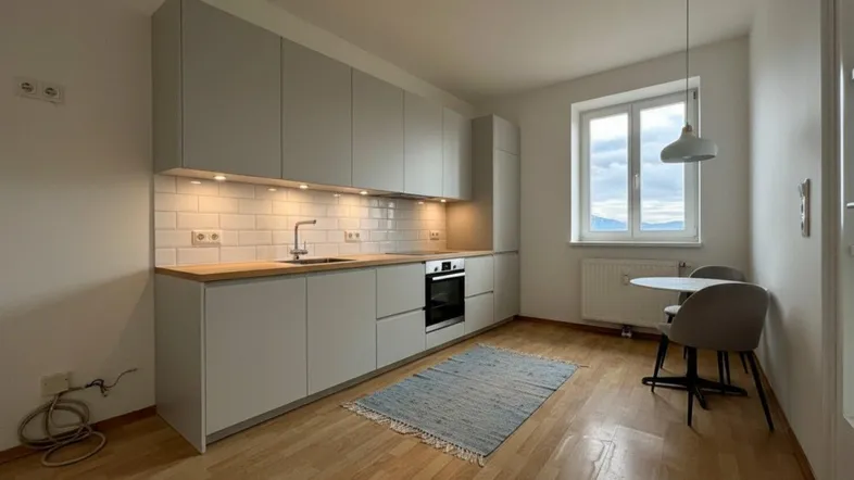 Helle Einbauküche mit modernen grauen Schränken, Holztheke und Essbereich am Fenster mit Bergblick.