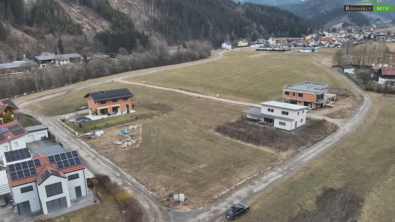 Luftaufnahme eines Wohngebiets mit mehreren Häusern und unbebauten Grundstücken in hügeliger Landschaft.