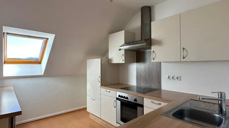 Helle Küche im Dachgeschoss mit Einbauküche, Holzoptik-Arbeitsplatte und Dachfenster.