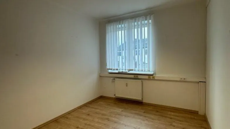 Heller Büroraum mit Laminatboden und einem Fenster, das natürliches Licht hereinlässt, ideal für Arbeitszwecke.