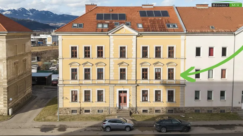 Historisches Gebäude mit gelber Fassade, roten Ziegeldächern und Solarpaneelen auf dem Dach.