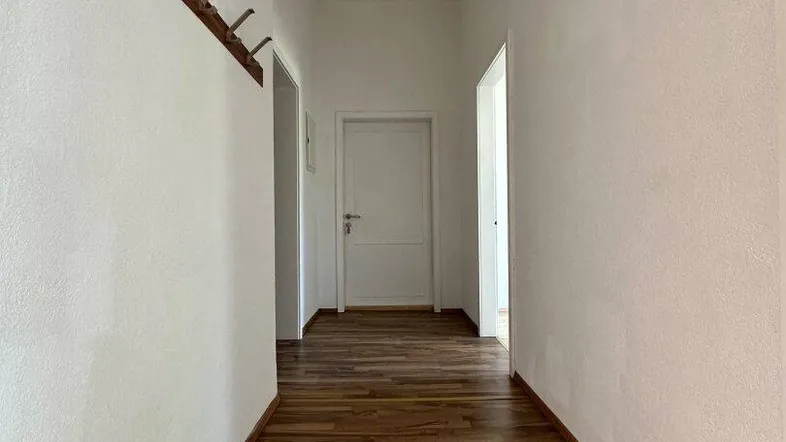 Langer Flur mit hellem Laminatboden und weißen Wänden, der zu weiteren Räumen führt.