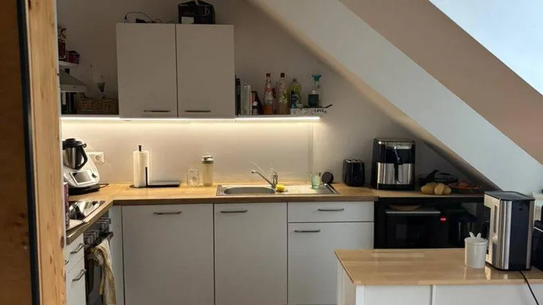 Moderne Küche im Dachgeschoss mit Holztheke, weißen Schränken und integrierter Beleuchtung unter den Oberschränken.