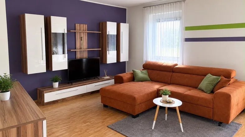 Modernes Wohnzimmer mit orangefarbenem Ecksofa, Holzboden und lila Akzentwand.