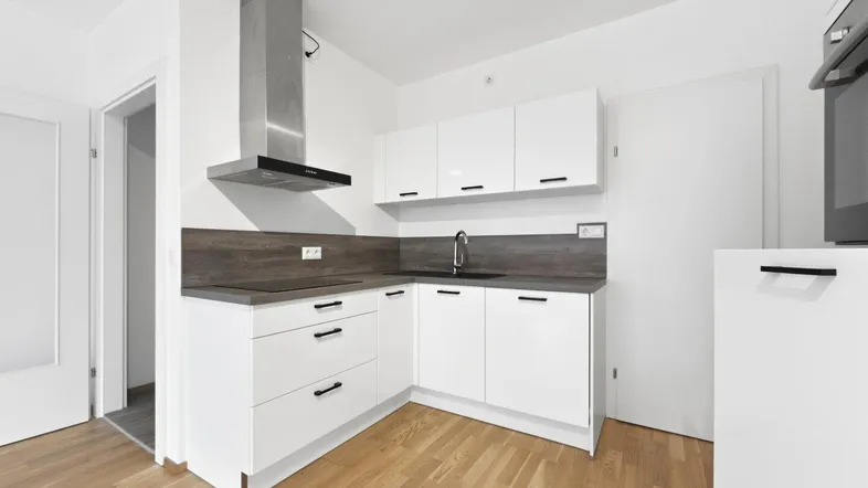 Moderne Einbauküche mit weißen Hochglanzfronten, Holzarbeitsplatte und Dunstabzugshaube in einem hellen Raum.