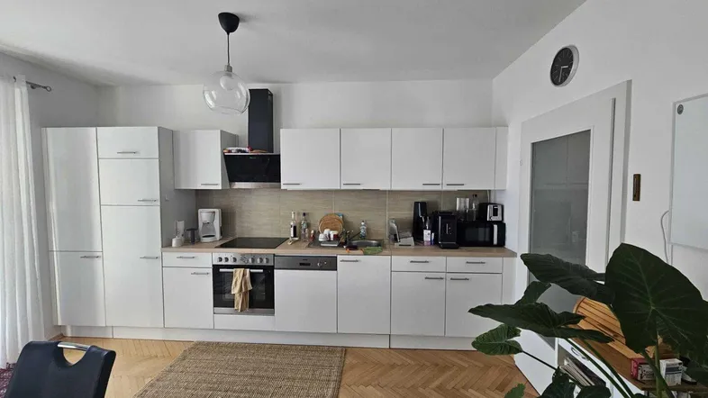 Moderne Einbauküche mit weißen Fronten, Holzarbeitsplatte und Fischgrätparkettboden.