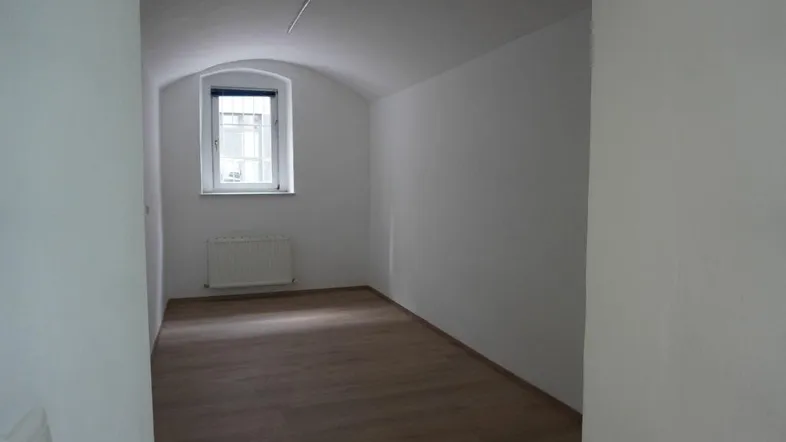 Heller Raum mit gewölbter Decke, einem Fenster und Laminatboden, ideal für verschiedene Nutzungen.
