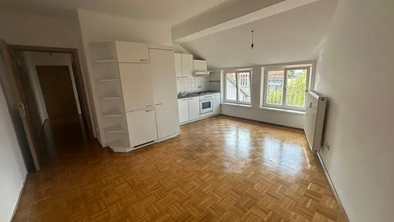 Helle Dachgeschosswohnung mit offener Küche, Parkettboden und Fenstern mit Blick ins Grüne.