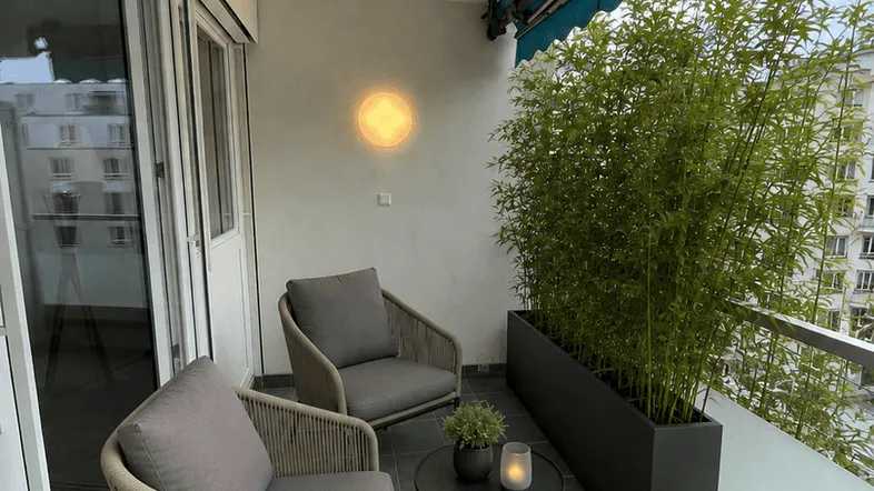 Gemütlicher Balkon mit modernen Sitzmöbeln, Pflanzenkübel und Blick auf die Stadtbebauung.