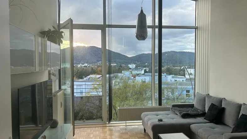 Helles Wohnzimmer mit großen Fenstern, Bergblick und modernem Sofa.