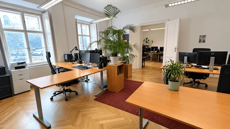 Geräumiges Büro mit mehreren Arbeitsplätzen, großen Fenstern und klassischem Fischgrätparkettboden.